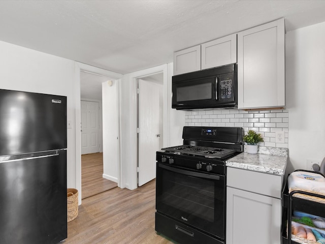 5536 Goodman Ave, Fort Worth, TX 76107 - kitchen featuring black appliances, light wood-type flooring, decorative backsplash, light stone counters, and white cabinetry