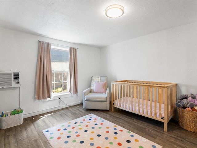 5536 Goodman Ave, Fort Worth, TX 76107 - bedroom with wood finished floors, an AC wall unit, a crib, and baseboards