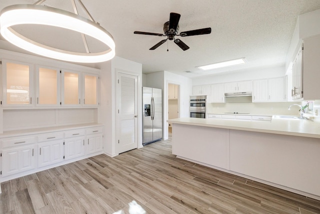 kitchen featuring light wood-style flooring, appliances with stainless steel finishes, a sink, and under cabinet range hood
