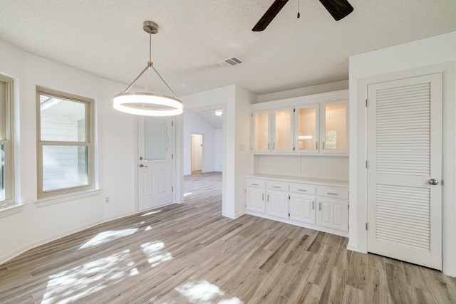 unfurnished dining area with visible vents, a ceiling fan, light wood-style floors, and a textured ceiling