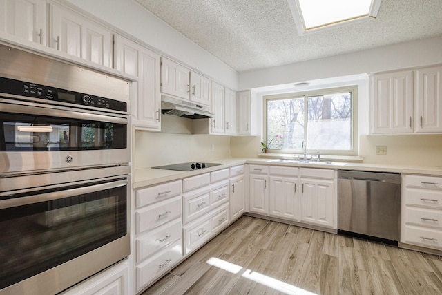 kitchen with white cabinetry, under cabinet range hood, light wood-style floors, stainless steel appliances, and a sink