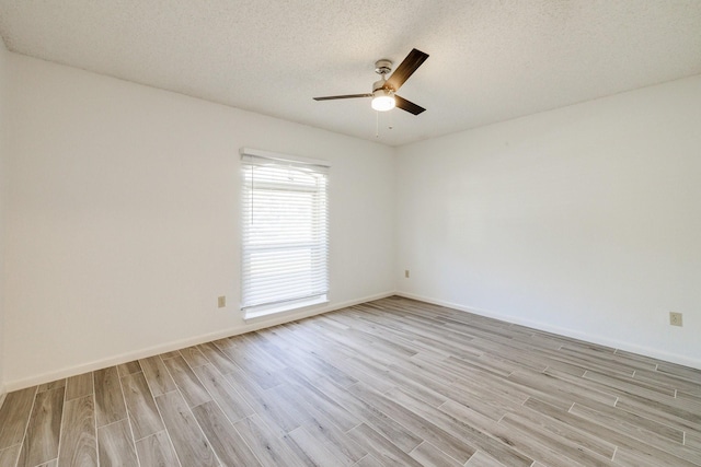 empty room with a textured ceiling, light wood finished floors, baseboards, and a ceiling fan