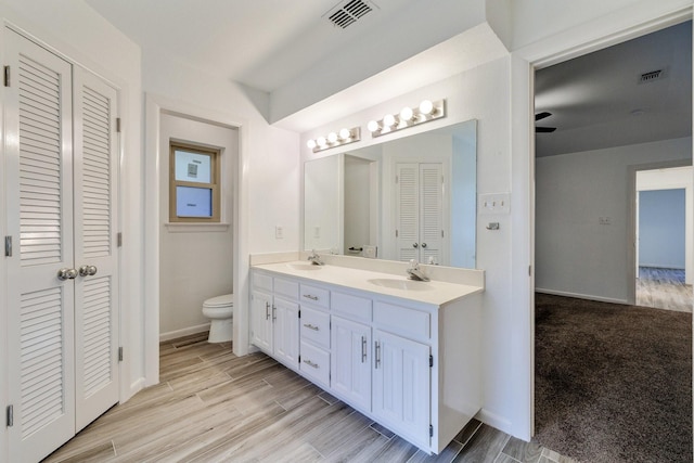 bathroom featuring toilet, a closet, a sink, and visible vents