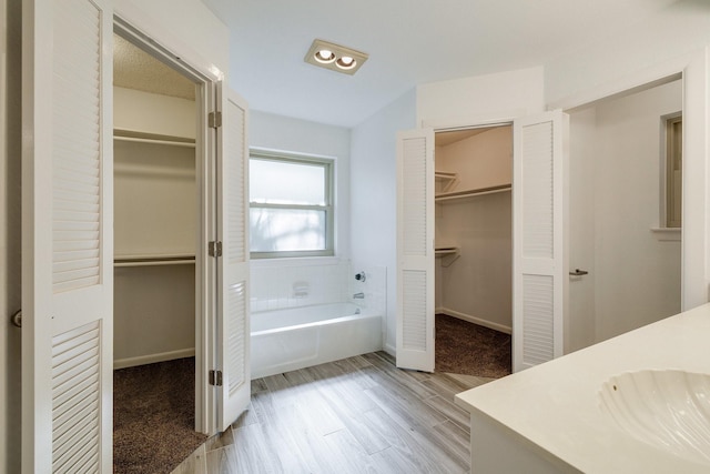 bathroom with a spacious closet, vanity, wood finished floors, and a garden tub