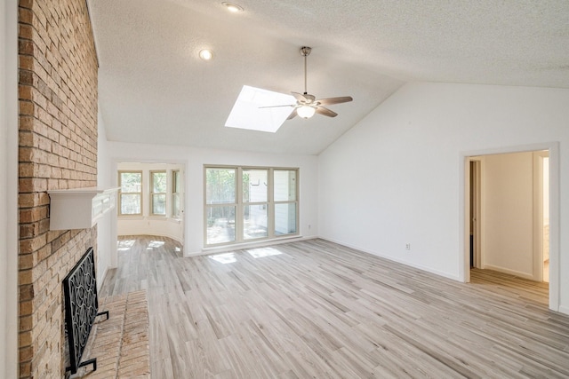 unfurnished living room featuring light wood-style floors, vaulted ceiling with skylight, ceiling fan, a textured ceiling, and a brick fireplace