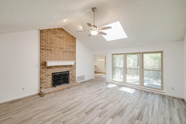 unfurnished living room with visible vents, vaulted ceiling with skylight, a brick fireplace, ceiling fan, and wood finished floors