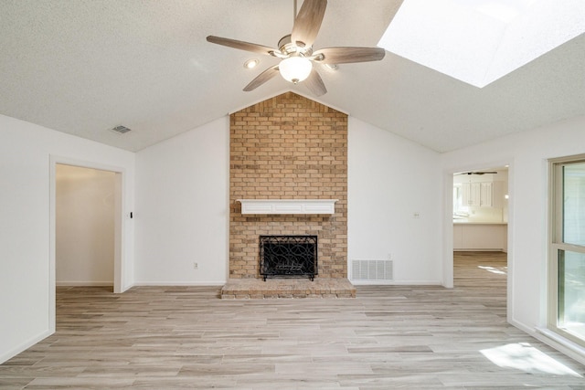 unfurnished living room with light wood finished floors, vaulted ceiling with skylight, ceiling fan, and visible vents