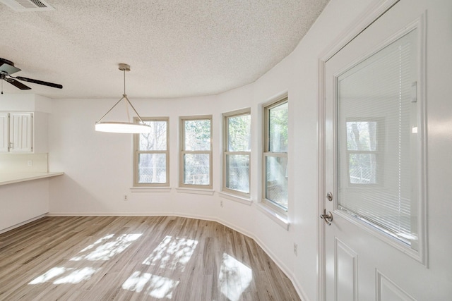 unfurnished dining area featuring visible vents, baseboards, light wood-style floors, and a textured ceiling