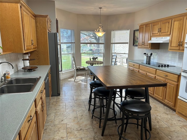 kitchen with a sink, stone tile floors, freestanding refrigerator, black electric stovetop, and under cabinet range hood