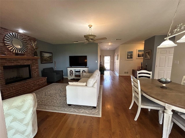 living room with wood finished floors, visible vents, baseboards, a fireplace, and ceiling fan