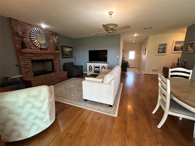 living room featuring a fireplace, wood finished floors, visible vents, and ceiling fan