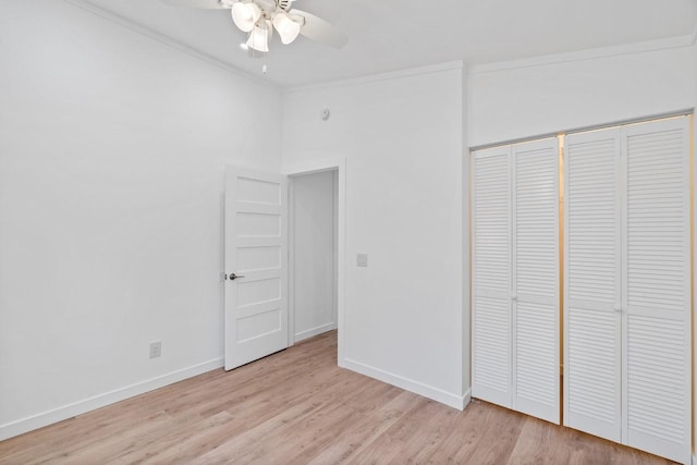 unfurnished bedroom featuring a ceiling fan, baseboards, light wood-style floors, a closet, and crown molding