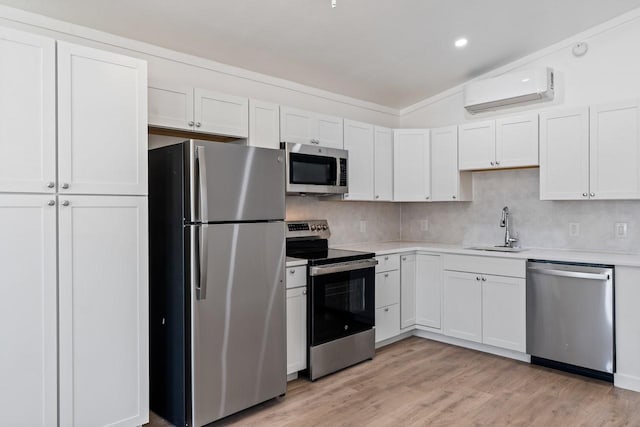 kitchen featuring light wood finished floors, a wall mounted air conditioner, light countertops, appliances with stainless steel finishes, and a sink