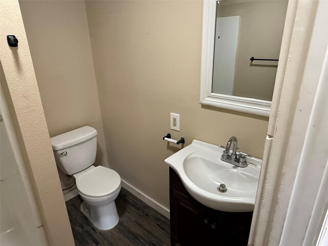 half bathroom with toilet, vanity, baseboards, and wood finished floors