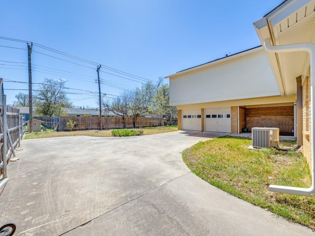 view of side of home with an attached garage, central AC unit, fence, and driveway