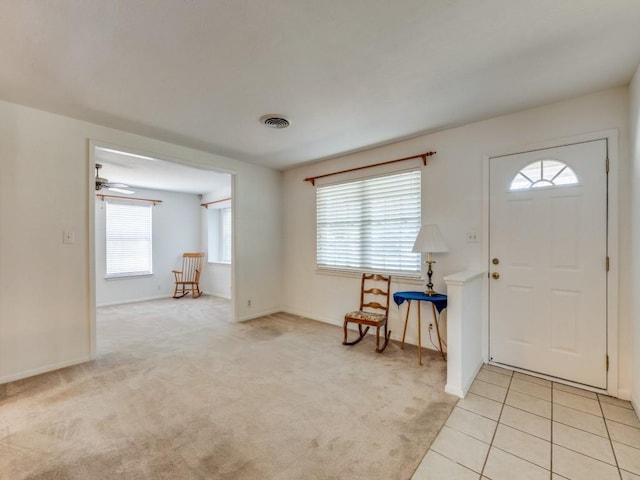 foyer featuring visible vents, baseboards, light carpet, light tile patterned floors, and a ceiling fan