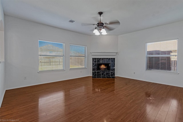 unfurnished living room featuring visible vents, baseboards, wood finished floors, a tiled fireplace, and a ceiling fan