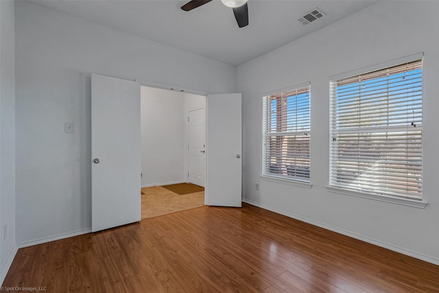 unfurnished room featuring baseboards, visible vents, wood finished floors, and ceiling fan