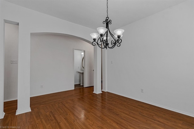 empty room featuring an inviting chandelier, arched walkways, baseboards, and wood finished floors