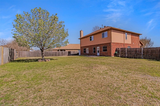 rear view of property featuring a fenced backyard, a lawn, a chimney, and brick siding