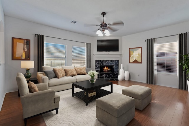 living room with visible vents, a tiled fireplace, wood finished floors, and ceiling fan