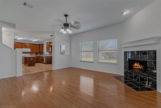 unfurnished living room with visible vents, a tiled fireplace, a ceiling fan, and wood finished floors
