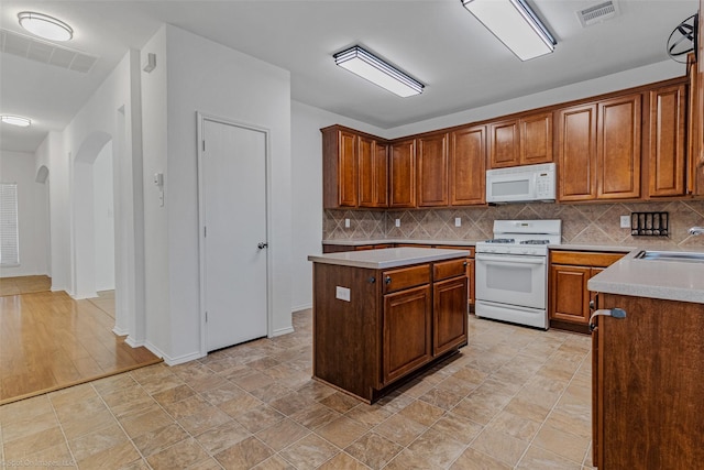 kitchen with arched walkways, visible vents, backsplash, and white appliances