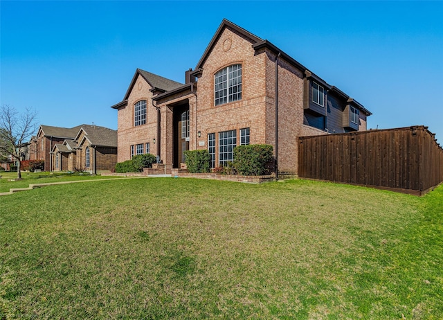 traditional-style house with brick siding, fence, and a front lawn