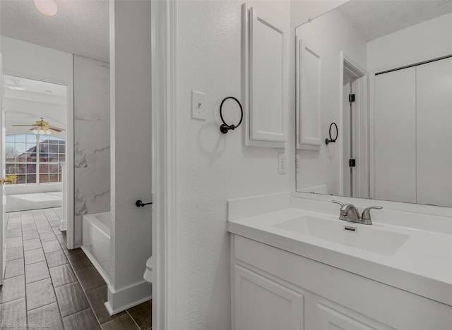 bathroom with a ceiling fan, vanity, toilet, and a textured ceiling