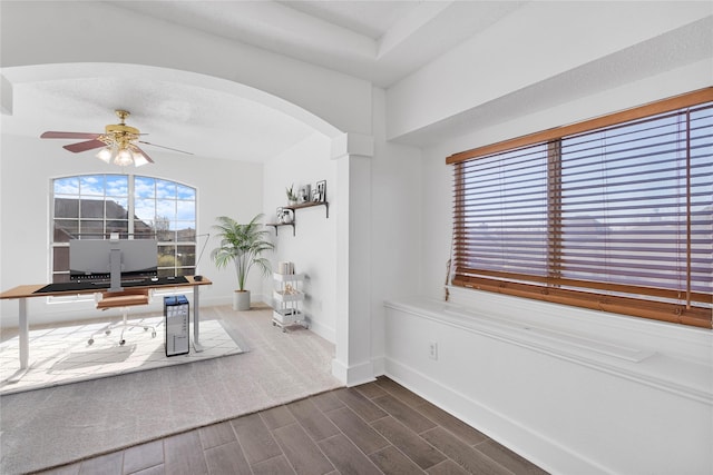 office featuring a ceiling fan, wood finish floors, arched walkways, and baseboards