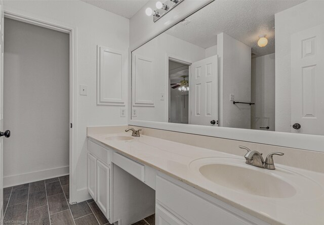 bathroom featuring baseboards, double vanity, a textured ceiling, and a sink