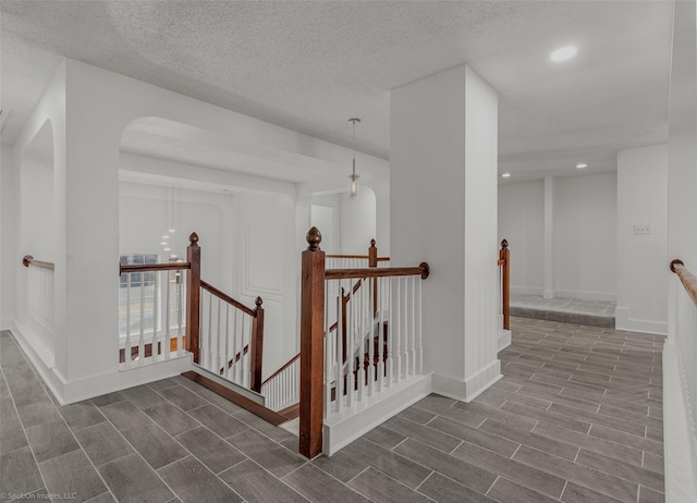 hall with an upstairs landing, wood finish floors, and recessed lighting