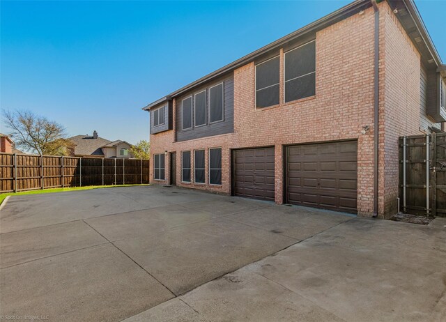 rear view of house with driveway, brick siding, a garage, and fence