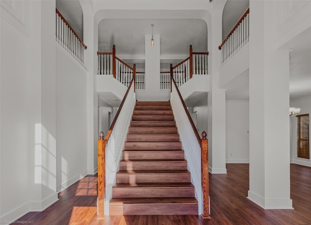 staircase with a towering ceiling, baseboards, and wood finished floors