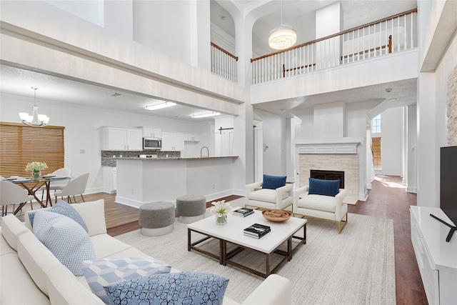 living area featuring baseboards, wood finished floors, a notable chandelier, and a stone fireplace