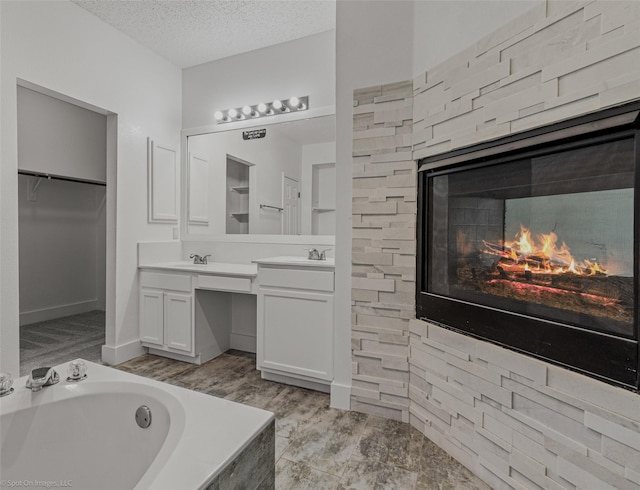 bathroom with vanity, a spacious closet, a textured ceiling, a multi sided fireplace, and a bath