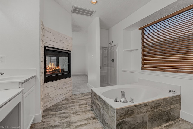 full bath with vanity, walk in shower, visible vents, a stone fireplace, and a bath