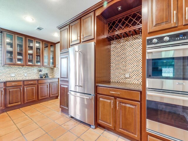 1410 Corto Dr, Dallas, TX 75218 - kitchen featuring appliances with stainless steel finishes, light tile patterned floors, tasteful backsplash, brown cabinets, and recessed lighting