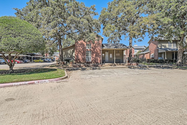 view of property hidden behind natural elements featuring uncovered parking and brick siding