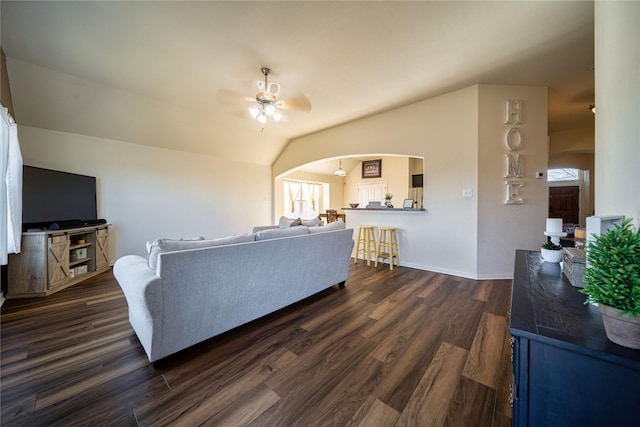 living room with baseboards, vaulted ceiling, arched walkways, a ceiling fan, and dark wood-style flooring