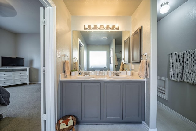full bath featuring double vanity, a textured wall, baseboards, and a sink