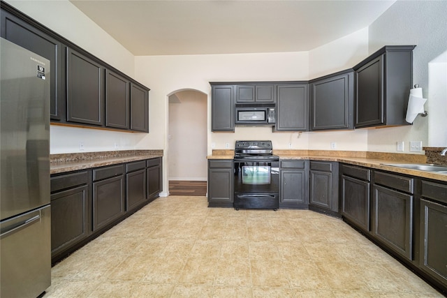 kitchen featuring a sink, baseboards, arched walkways, and black appliances