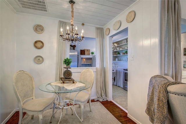 dining space featuring visible vents, crown molding, built in shelves, wood finished floors, and an inviting chandelier