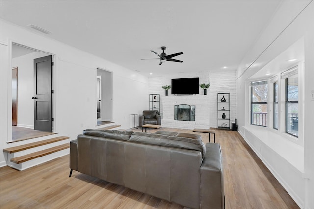 living area with visible vents, a brick fireplace, baseboards, light wood-style floors, and a ceiling fan