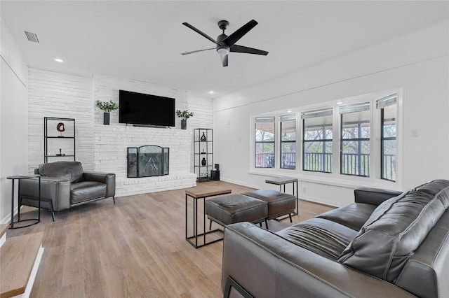 living area featuring light wood-type flooring, visible vents, a brick fireplace, and ceiling fan