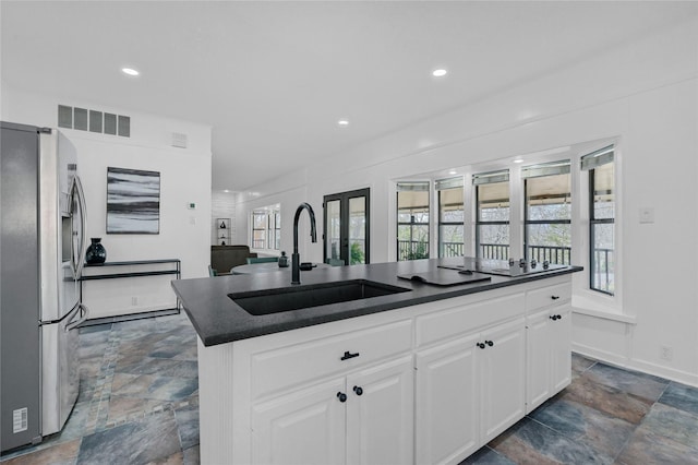 kitchen featuring visible vents, stainless steel fridge with ice dispenser, a sink, stone finish flooring, and dark countertops