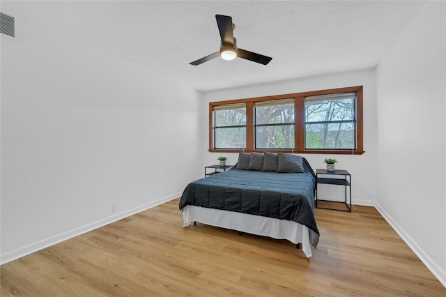 bedroom featuring baseboards, a textured ceiling, a ceiling fan, and light wood finished floors
