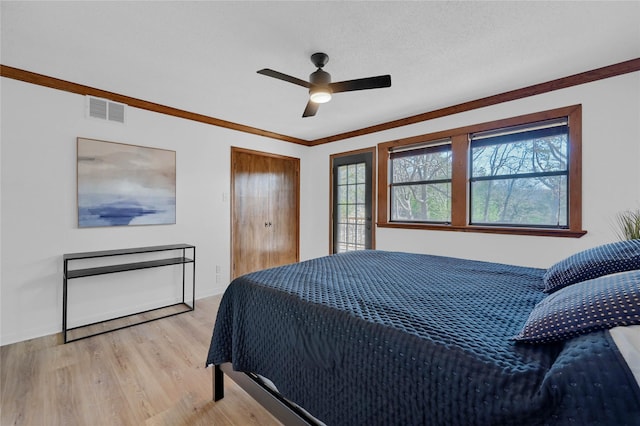 bedroom featuring visible vents, baseboards, light wood-type flooring, ornamental molding, and a ceiling fan