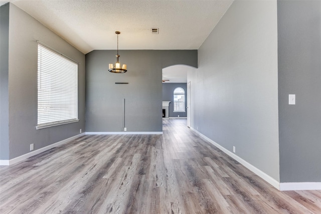 unfurnished dining area featuring arched walkways, wood finished floors, a textured ceiling, baseboards, and a chandelier