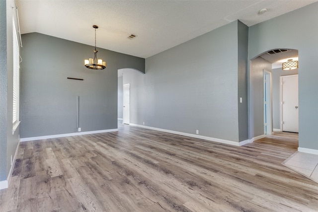 empty room with arched walkways, vaulted ceiling, wood finished floors, and a chandelier